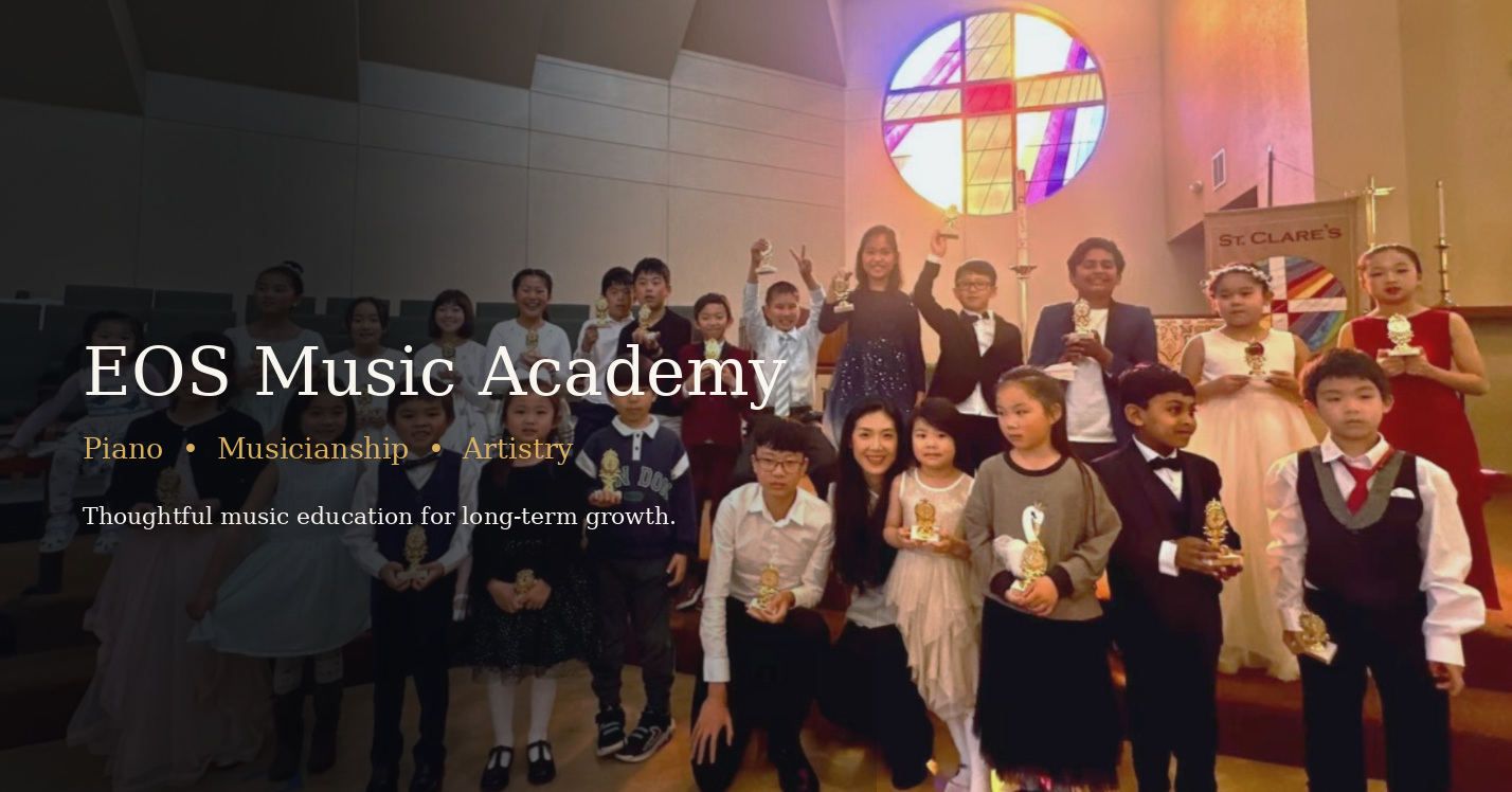 Group of children and adults on stage at a music academy, holding awards, in a church or concert hall with stained glass window and candles in the background.