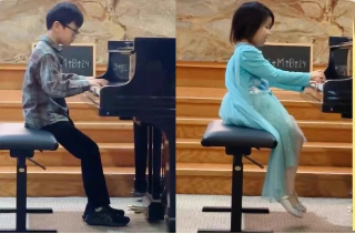 Two children, a boy and a girl, sitting side by side, playing pianos on a stage, with the boy on the left and the girl on the right.