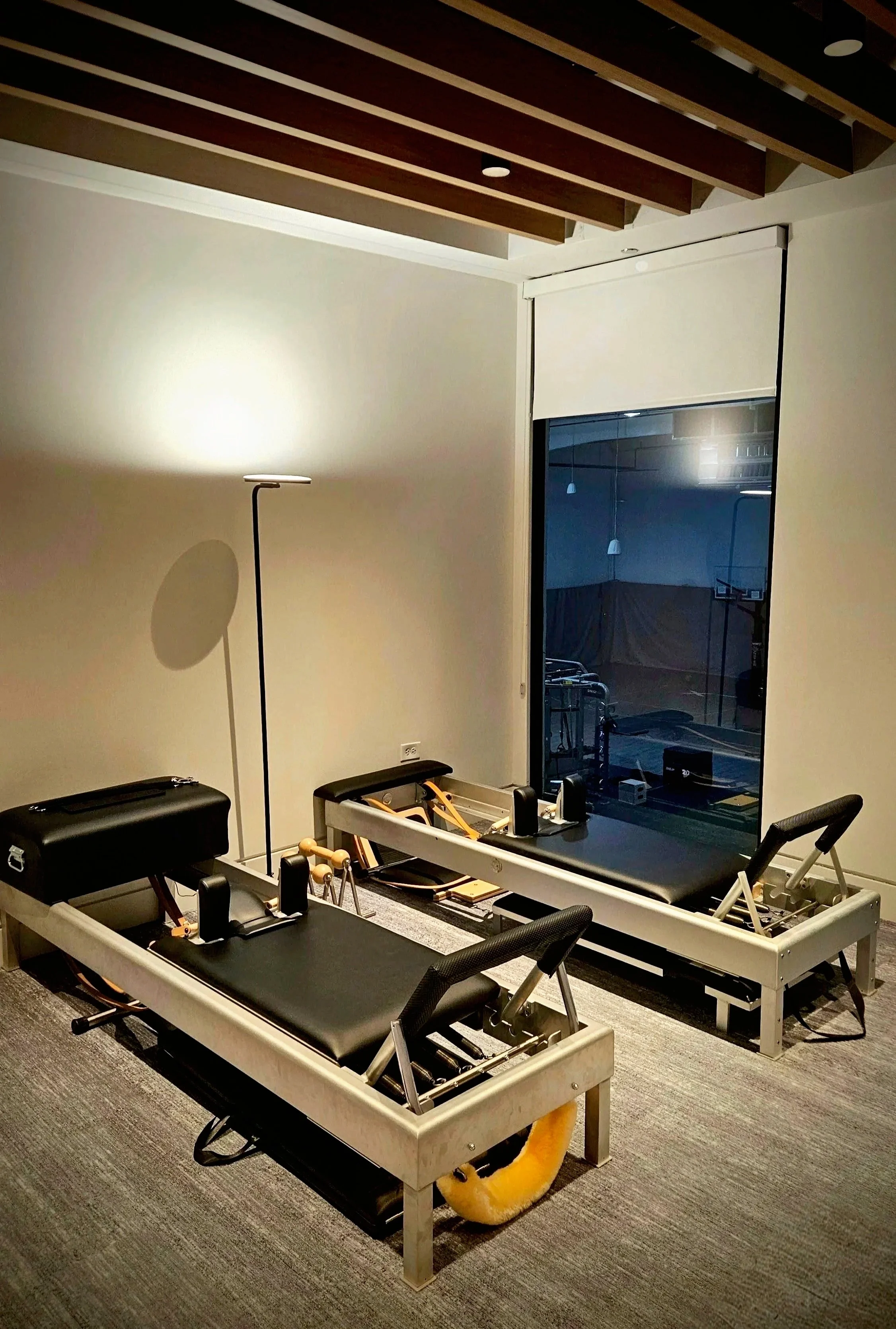 Pilates  studio with two classical Pilates reformers, a floor lamp, and exercise equipment near a sliding glass door.