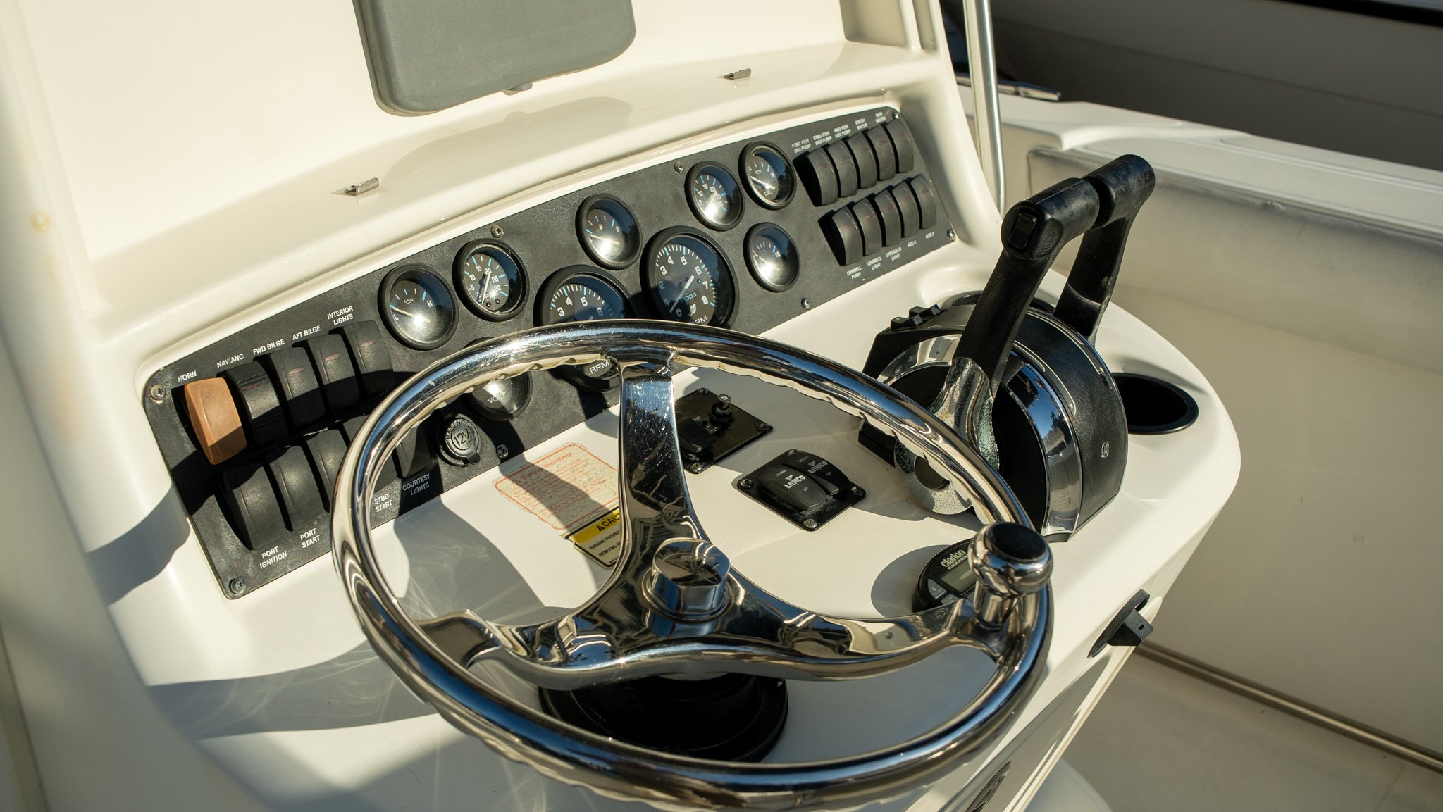 Close-up of the dashboard and steering wheel of a boat, featuring various gauges, switches, and controls.