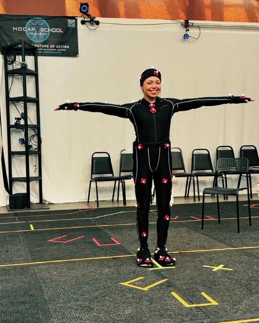 Woman wearing motion capture suit with markers, standing with arms outstretched in a studio, likely for film or animation reference.