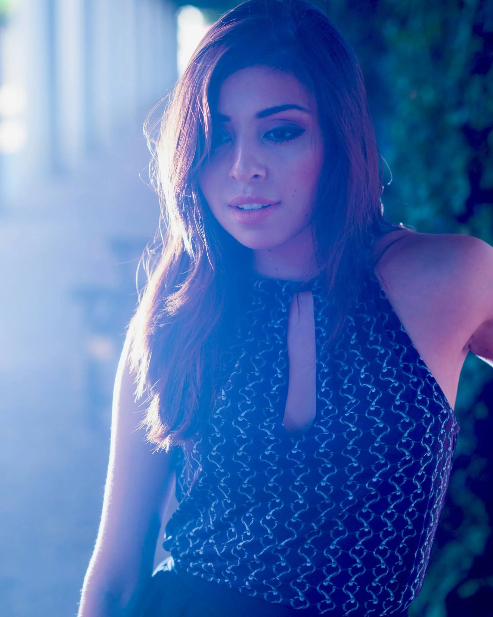 Close-up of a young woman outdoors, with sunlight illuminating her face and hair, wearing a patterned sleeveless top.