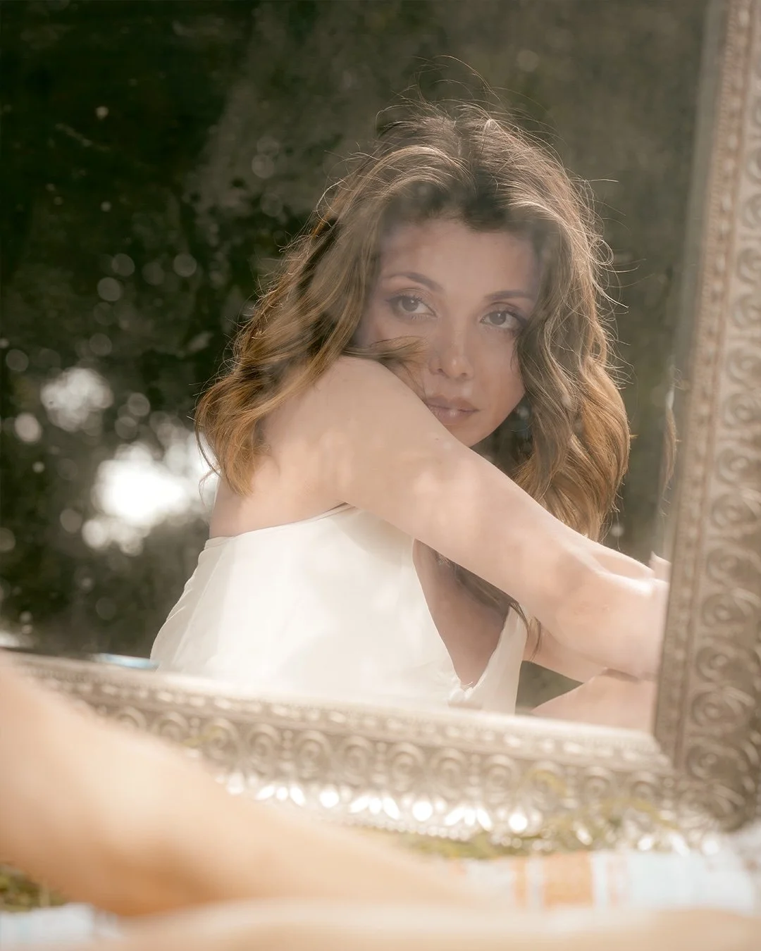 A woman with wavy brown hair looking into a mirror.