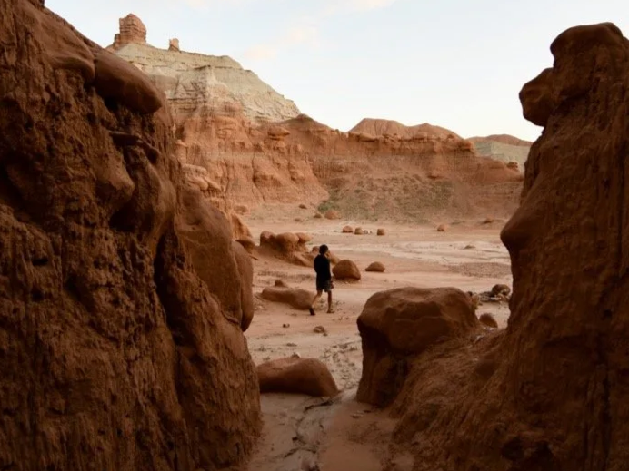 Diego Velasquez hiking in a desert canyon with red rock formations and cliffs in the background.