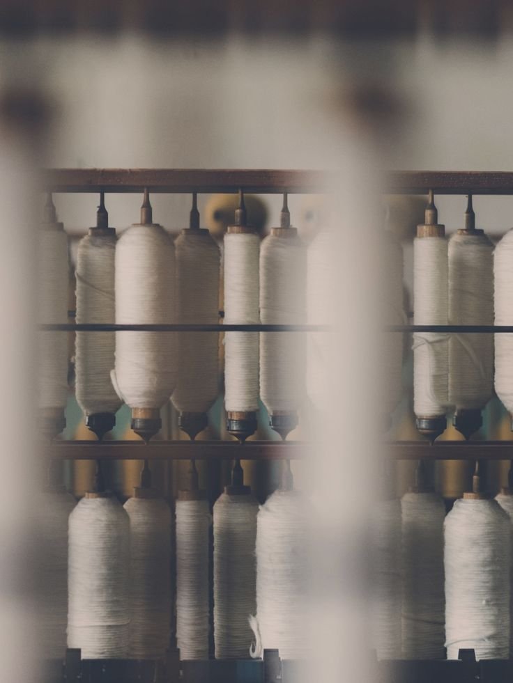 Close-up view of multiple white spools of thread on a weaving machine with a blurred background.