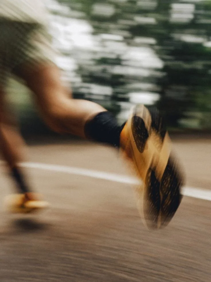 A person rollerblading outdoors on a paved surface, blurred due to motion, with trees in the background.