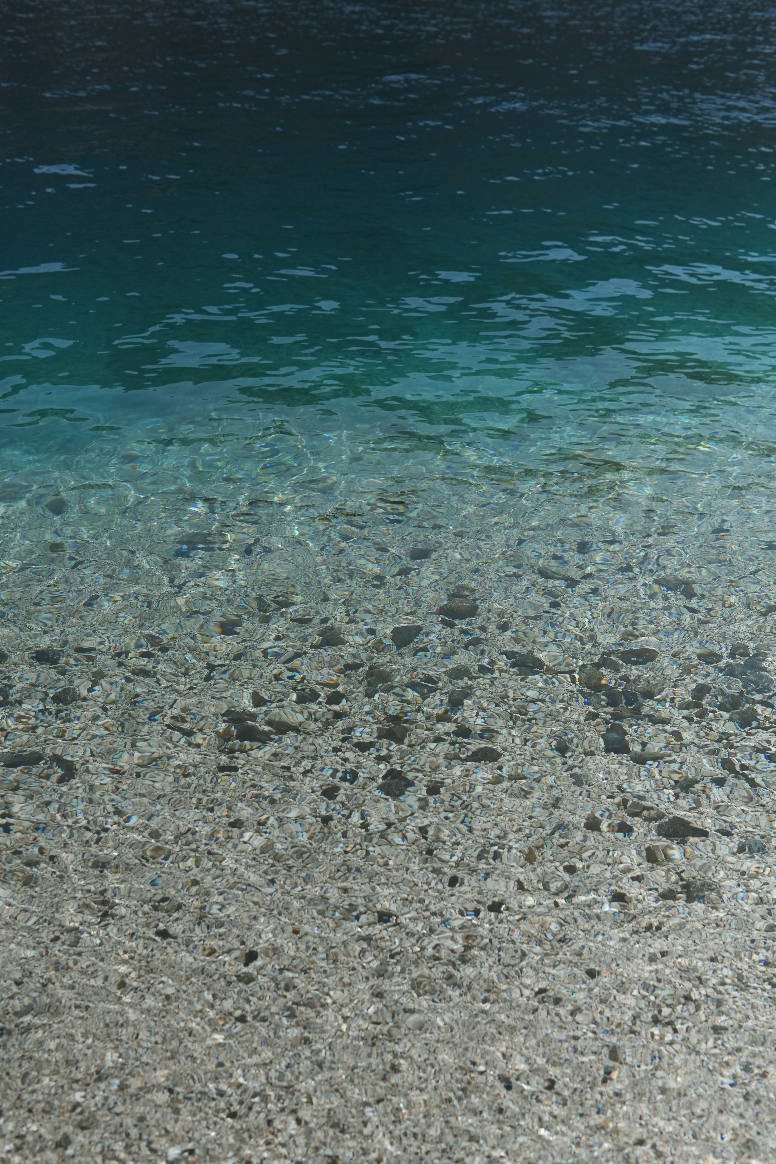 Clear water with pebbles at the bottom, transitioning from shallow to deeper water