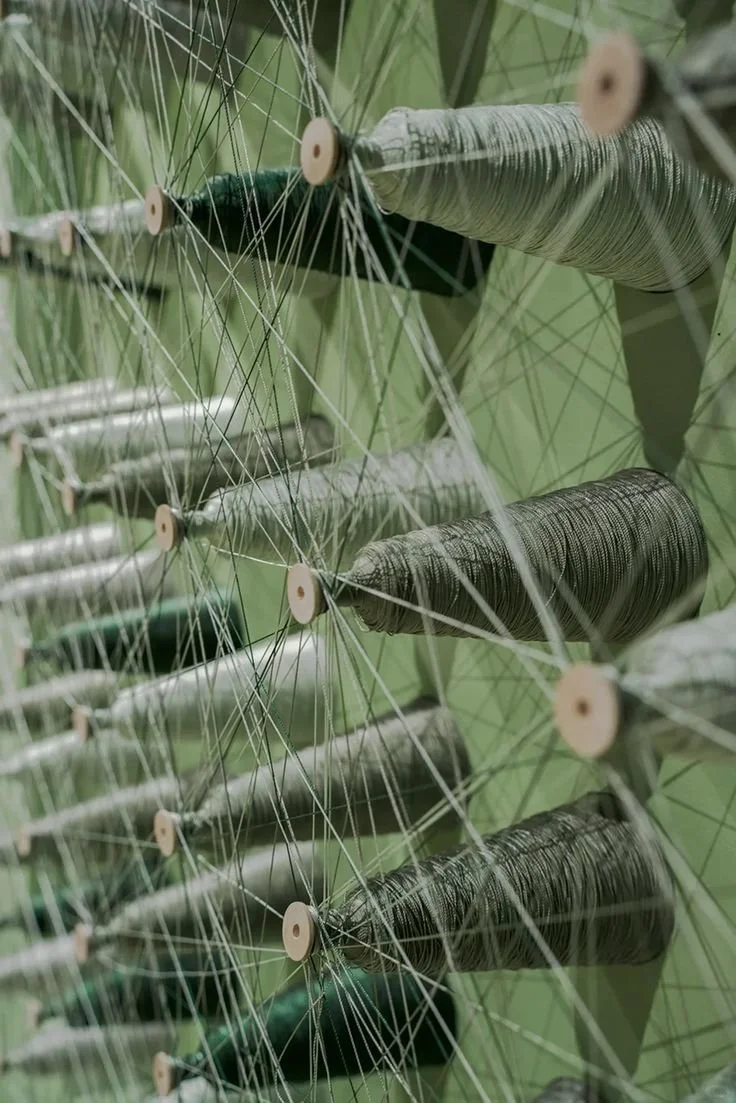 Multiple spools of gray thread mounted on a sewing machine with green background.