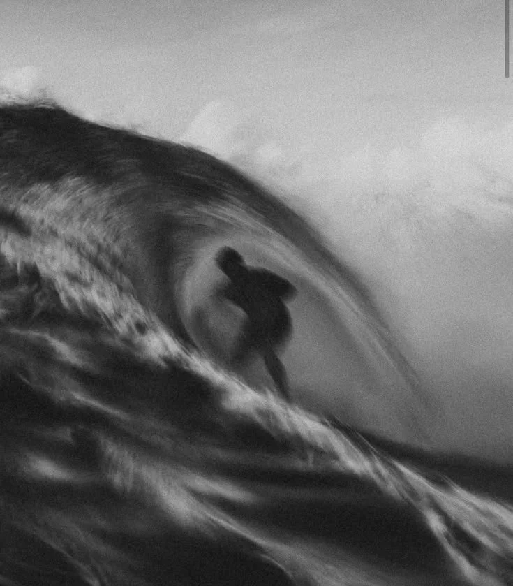 A person surfing on a large wave, viewed from the side, in black and white.