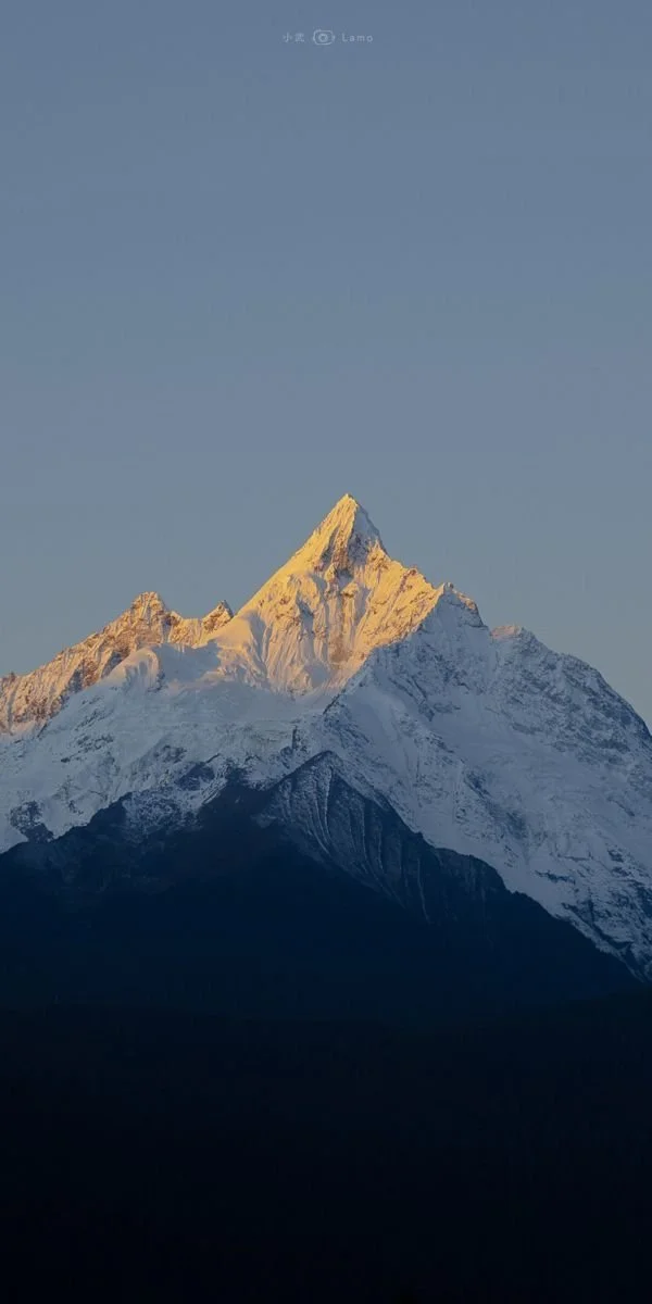 Snow-covered mountain peak illuminated by sunlight against a clear blue sky.
