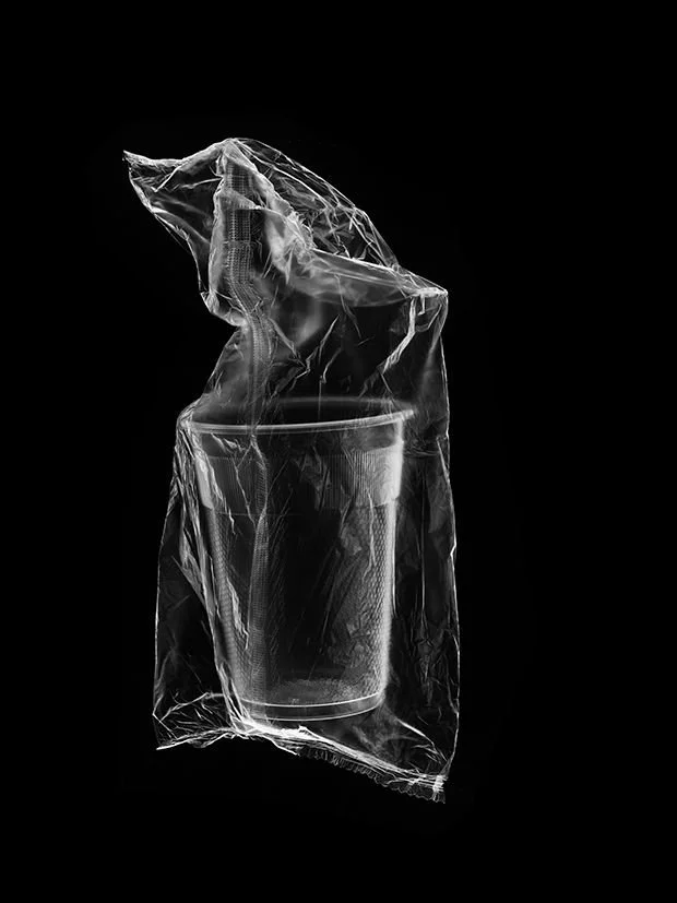 A plastic cup inside a crumpled plastic bag on a black background.