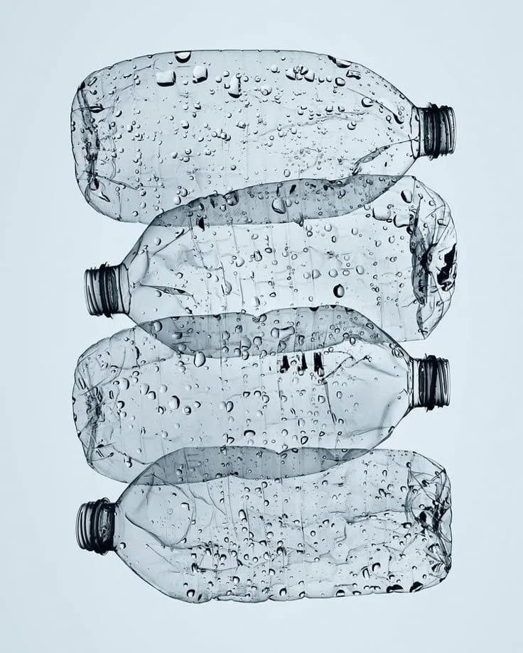 Four crumpled, transparent plastic water bottles with water droplets on their surface, lying horizontally.