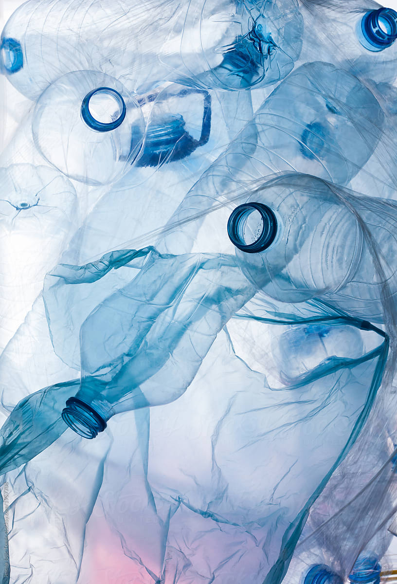 A collection of overturned clear plastic bottles with blue caps, some crumpled and overlapping, on a light background.