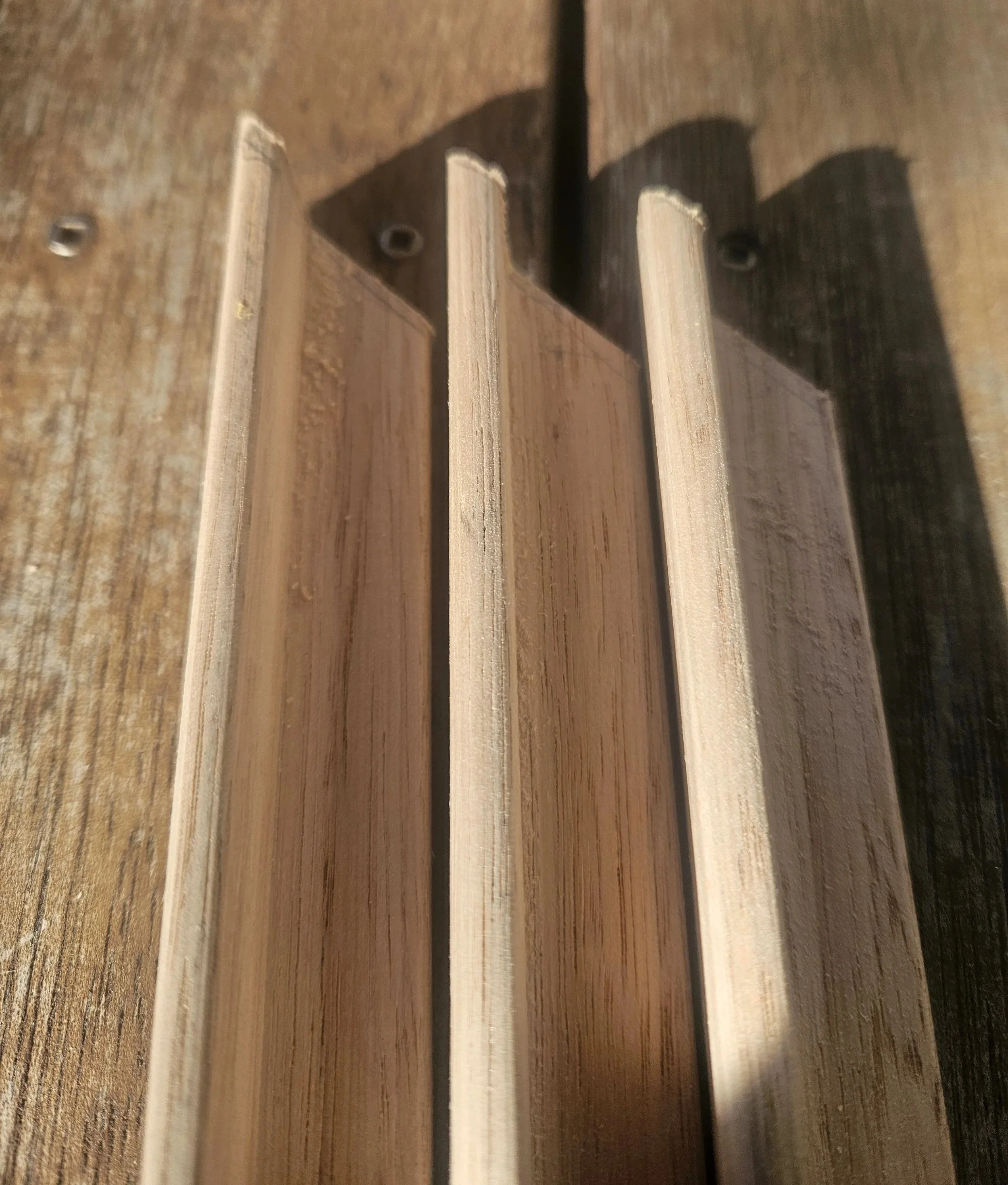 Close-up image of layered wooden planks or boards, some with visible screws, in varying shades of brown, with shadows cast on the surface.