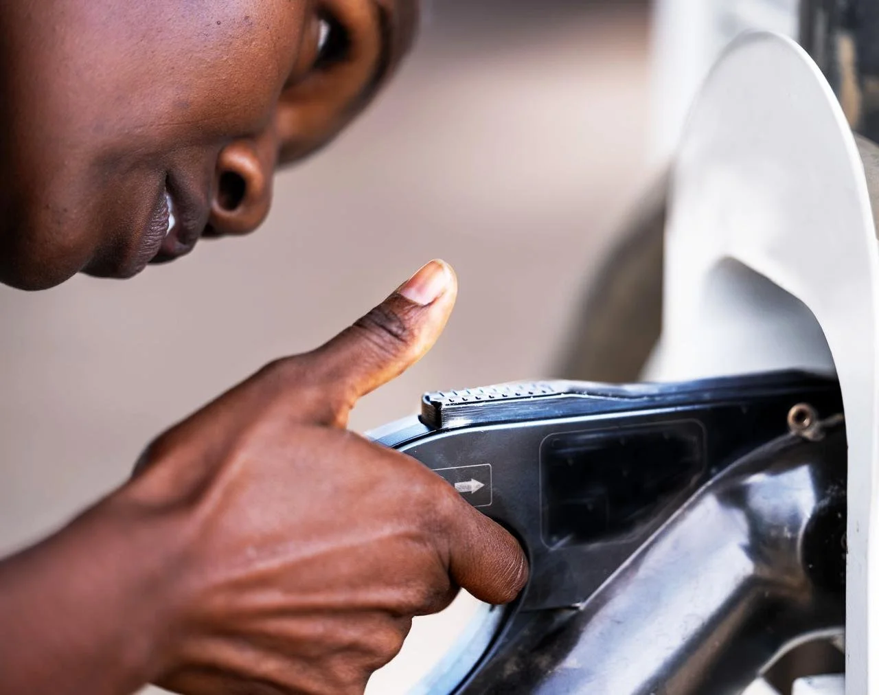 A person with dark skin is using a portable payment terminal inserted into an outdoor ATM machine.