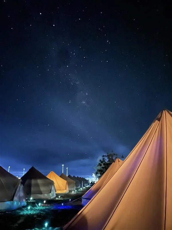 Nighttime view of camping tents under clear starry sky.