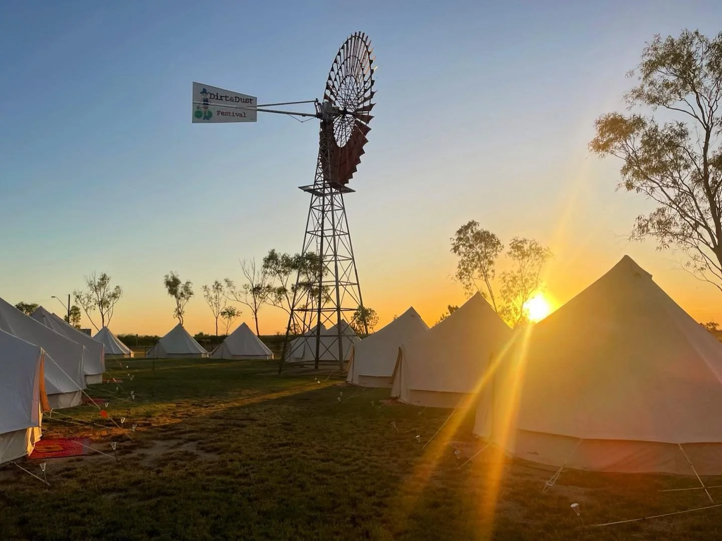 Sunset over a field of white tents at a festival with a windmill in the background.