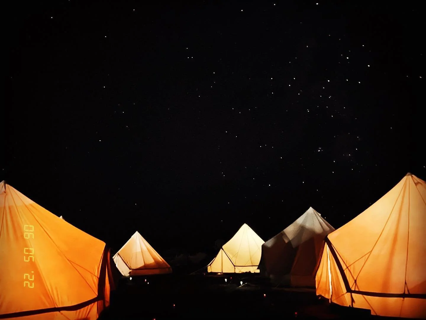 Nighttime scene of glowing tents set up outdoors beneath a starry sky.