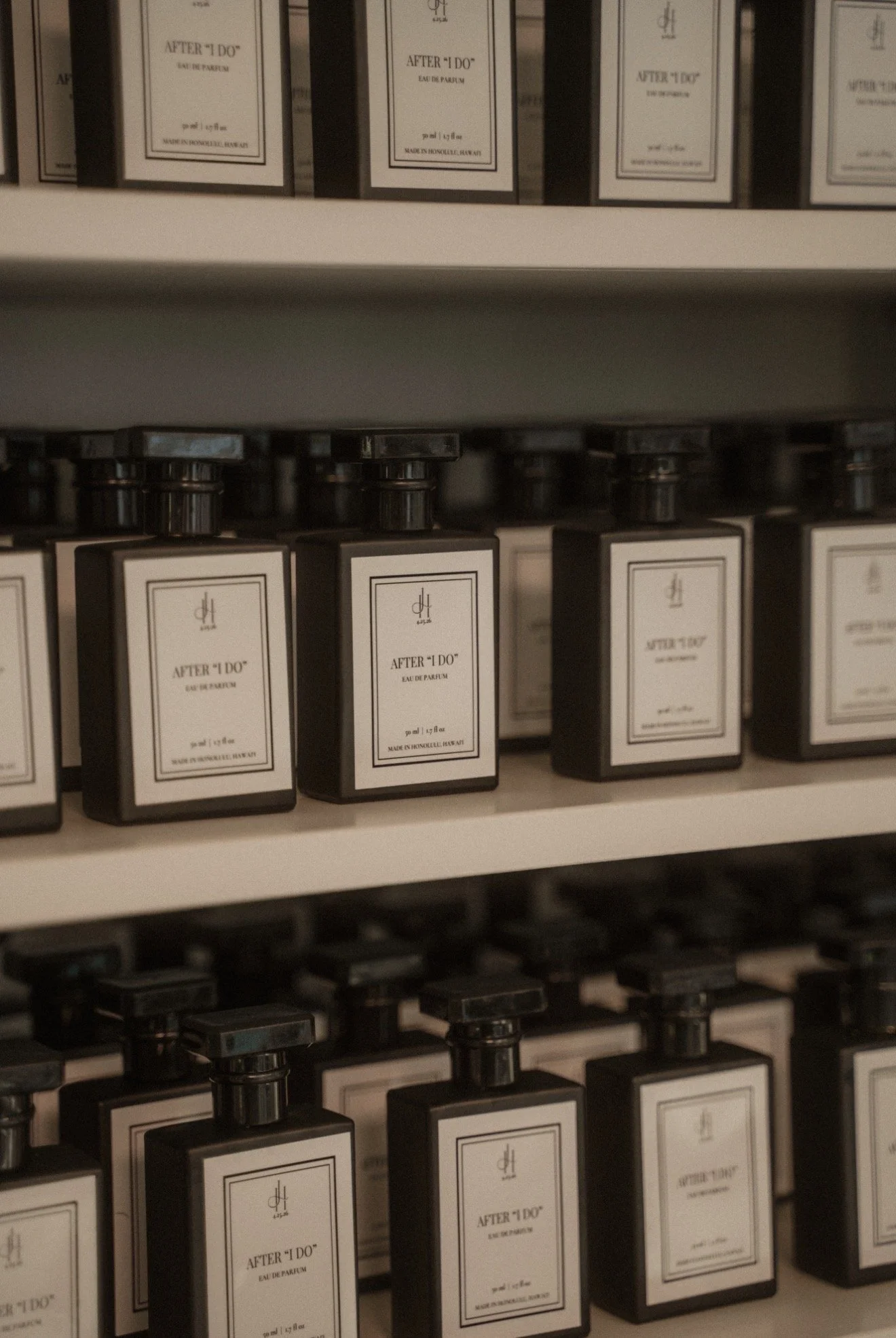 Shelf filled with bottles of 'After 'I Do' Eau de Parfum, with white labels and black caps, arranged in rows.