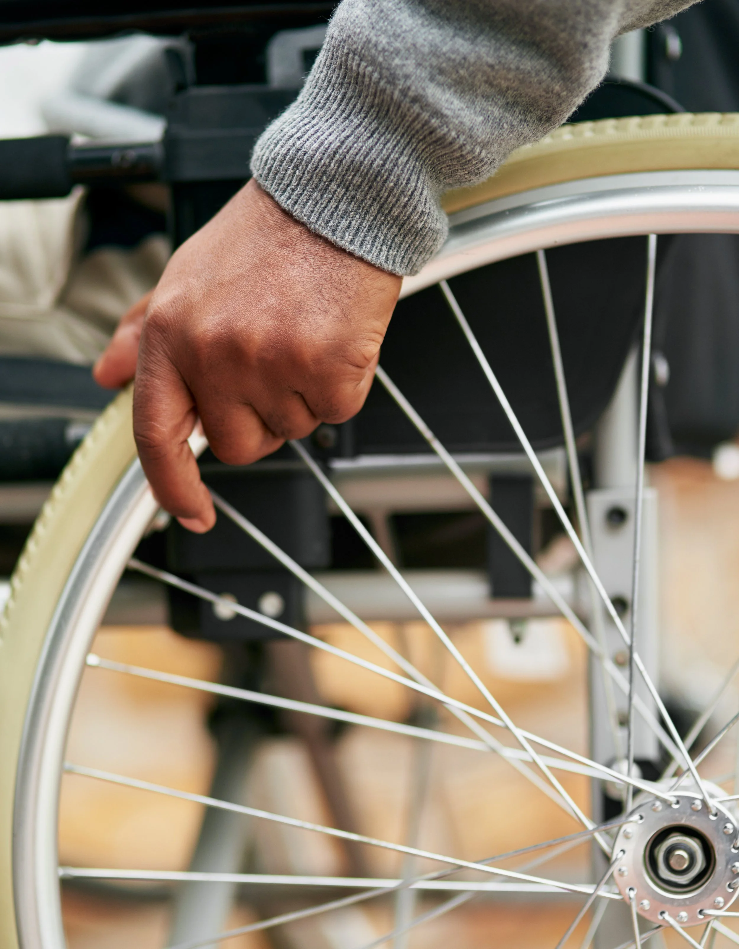 A person's hand holding a bicycle wheel with spokes, part of a grey long sleeve shirt visible, indoors.