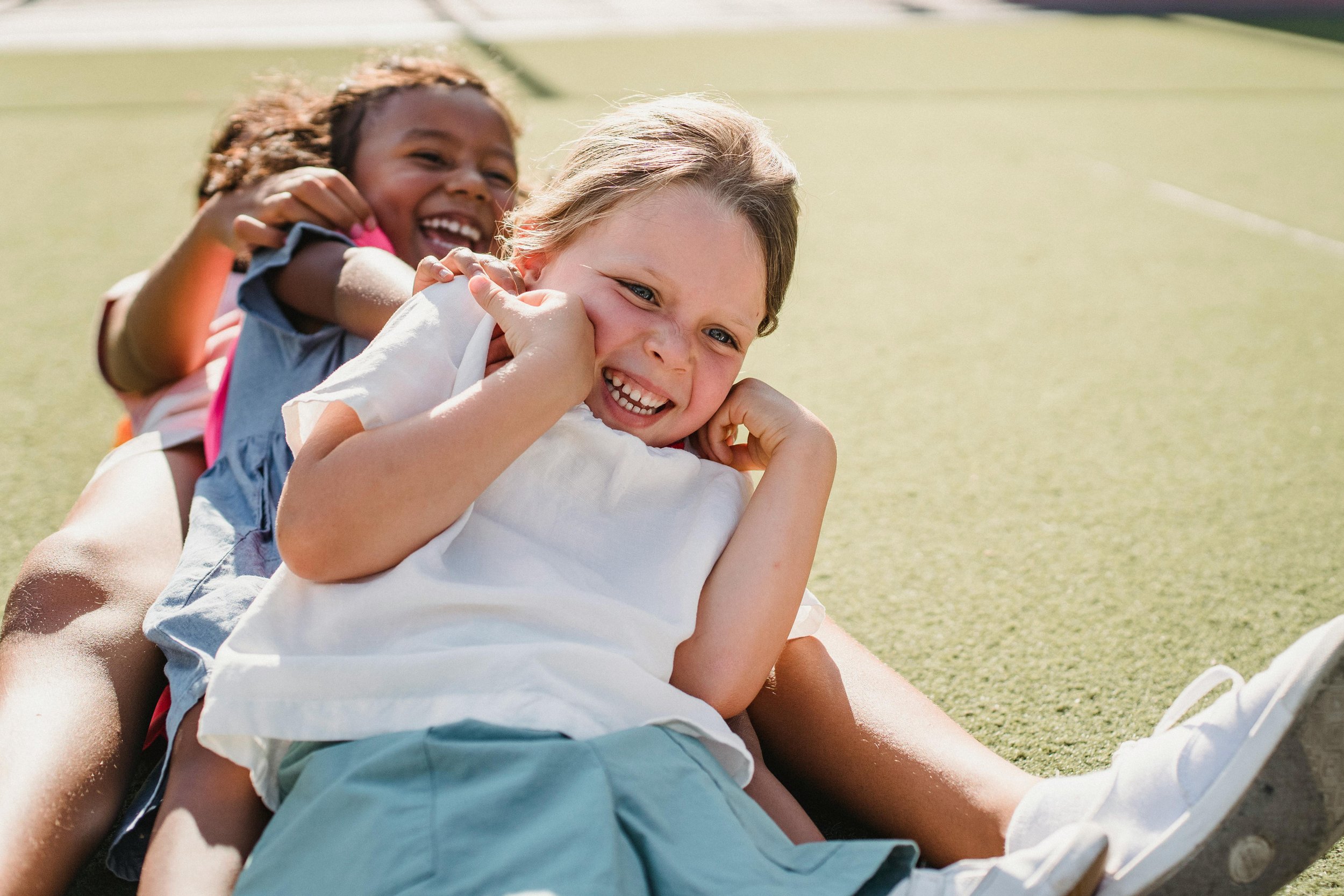 Three children playing together on a grassy field, laughing and smiling, enjoying outdoor fun.