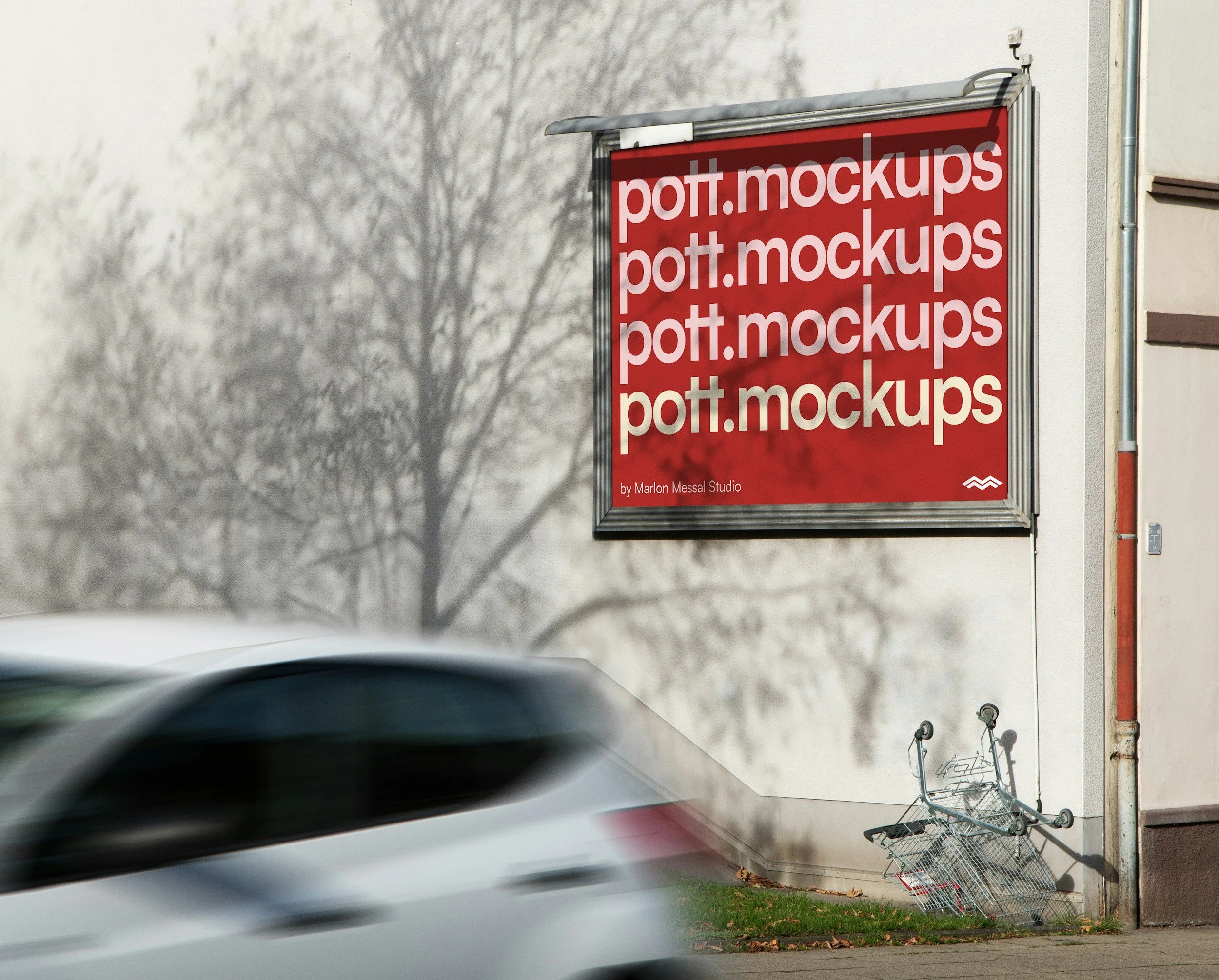 A red billboard with white text reading 'pott.mockups' is attached to an outdoor wall. There is a shadow of a leafless tree on the wall. A shopping cart is tipped over on the sidewalk, and a bicycle is lying on its side nearby. Part of a moving vehicle is blurred in the foreground.