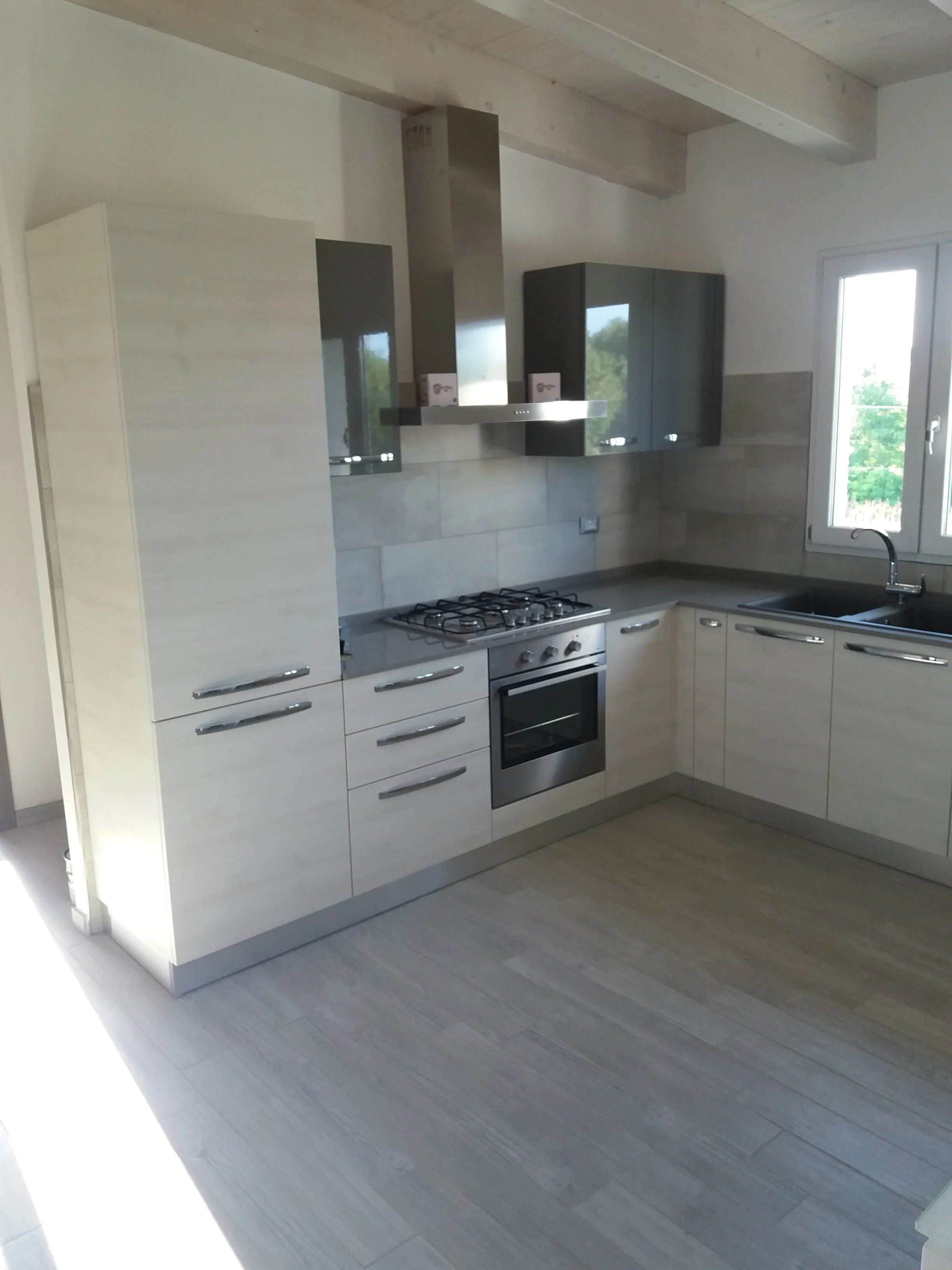 Modern kitchen with white cabinets, stainless steel stove and oven, gray countertops, and a window with a view of trees outside.