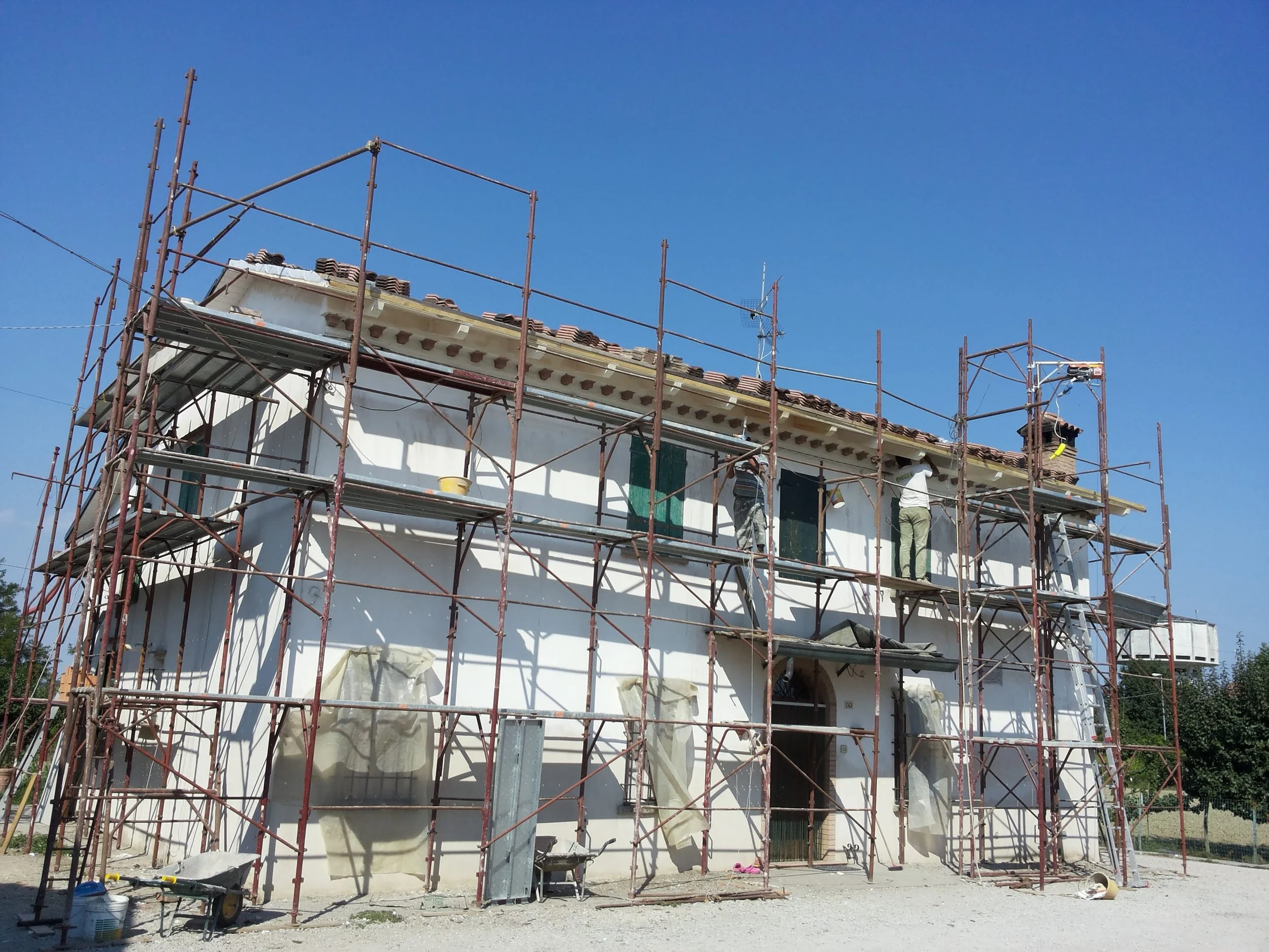 A house under construction with scaffolding surrounding it under a clear blue sky.