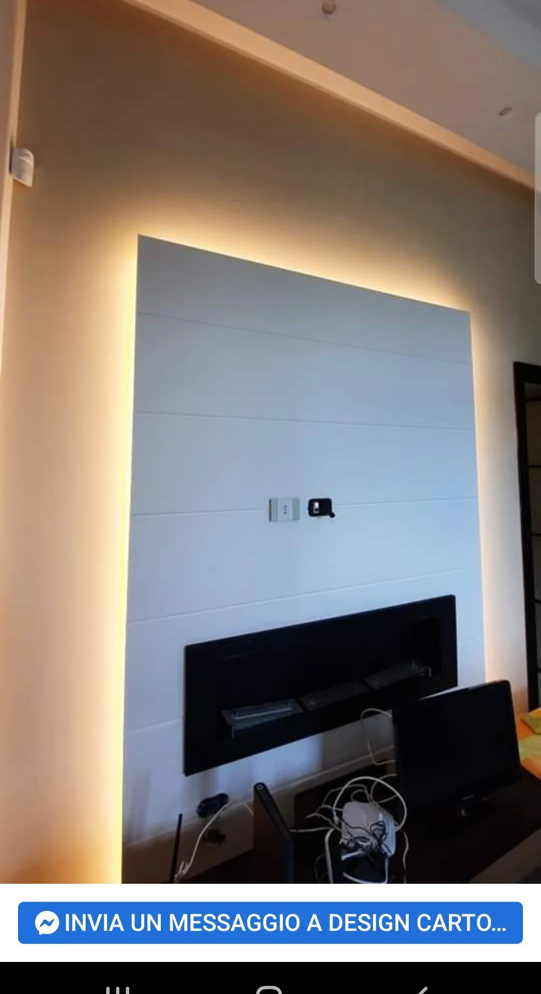A modern interior wall with indirect lighting behind a white panel and a mounted television displaying wires and electronic equipment below.