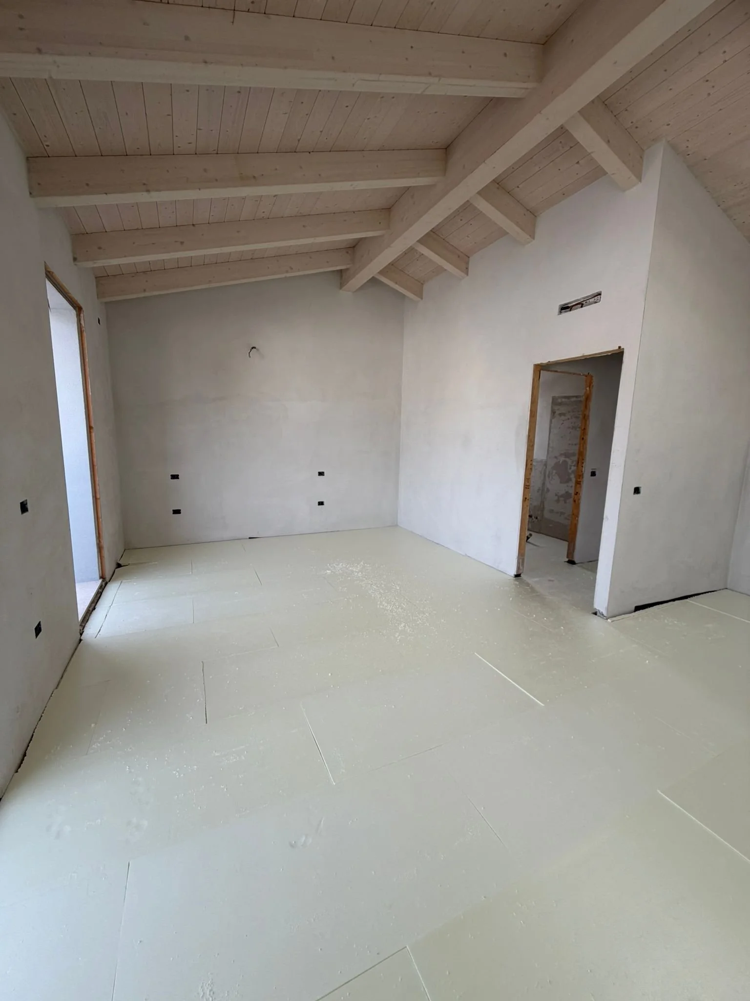 Empty room under construction with partially installed drywall, a wooden ceiling with exposed beams, and a light-colored floor.