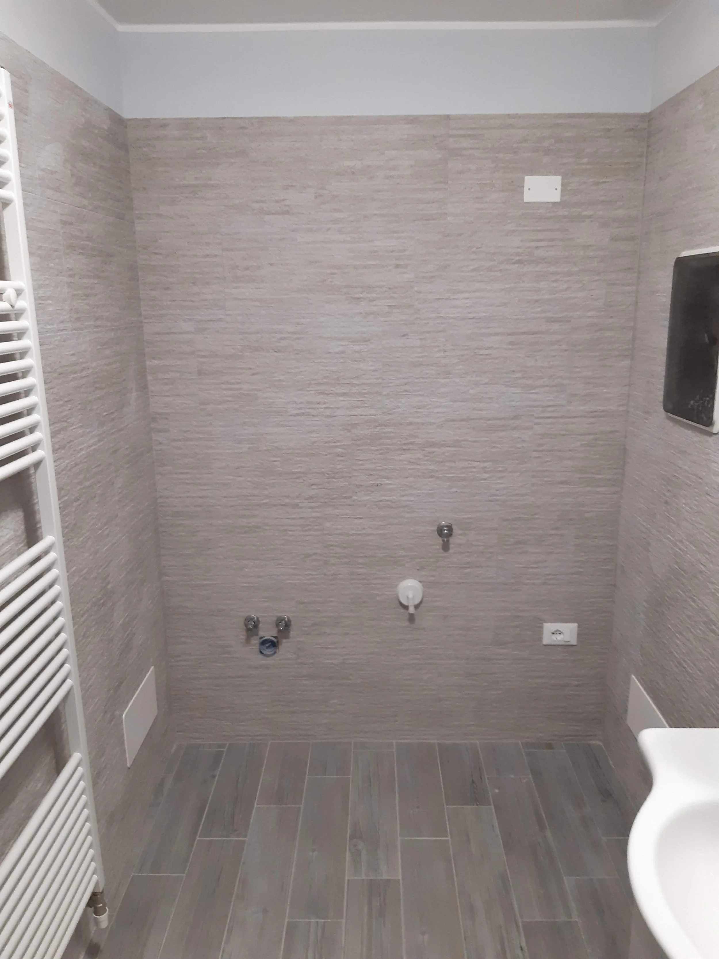 Unfinished bathroom or laundry room with tiled walls and floor, with plumbing and electrical outlets visible, but no fixtures or appliances installed.
