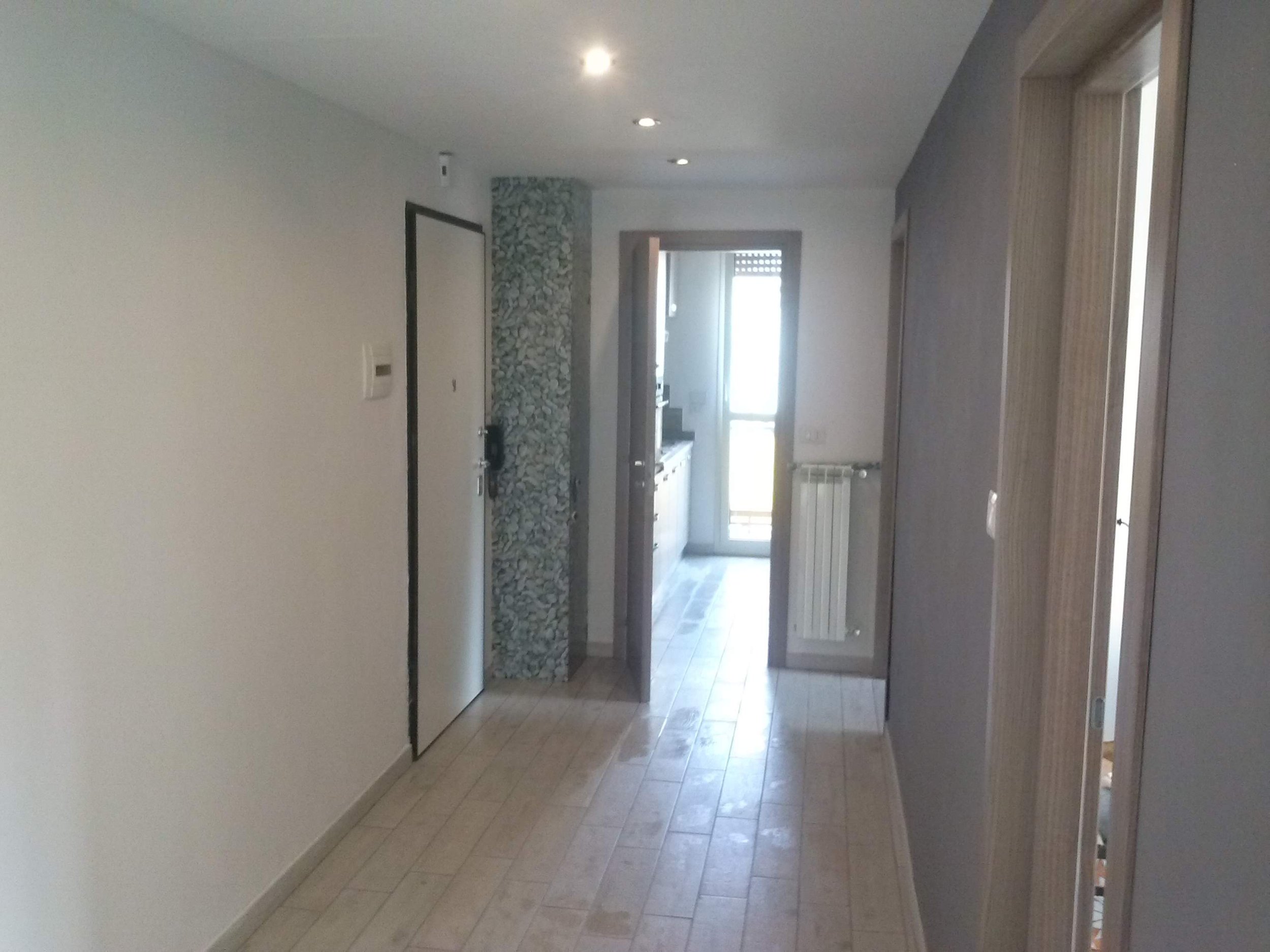 Interior view of a room with tiled floor, white walls, and a door leading outside. There are recessed ceiling lights and a stone decorative feature on the wall.