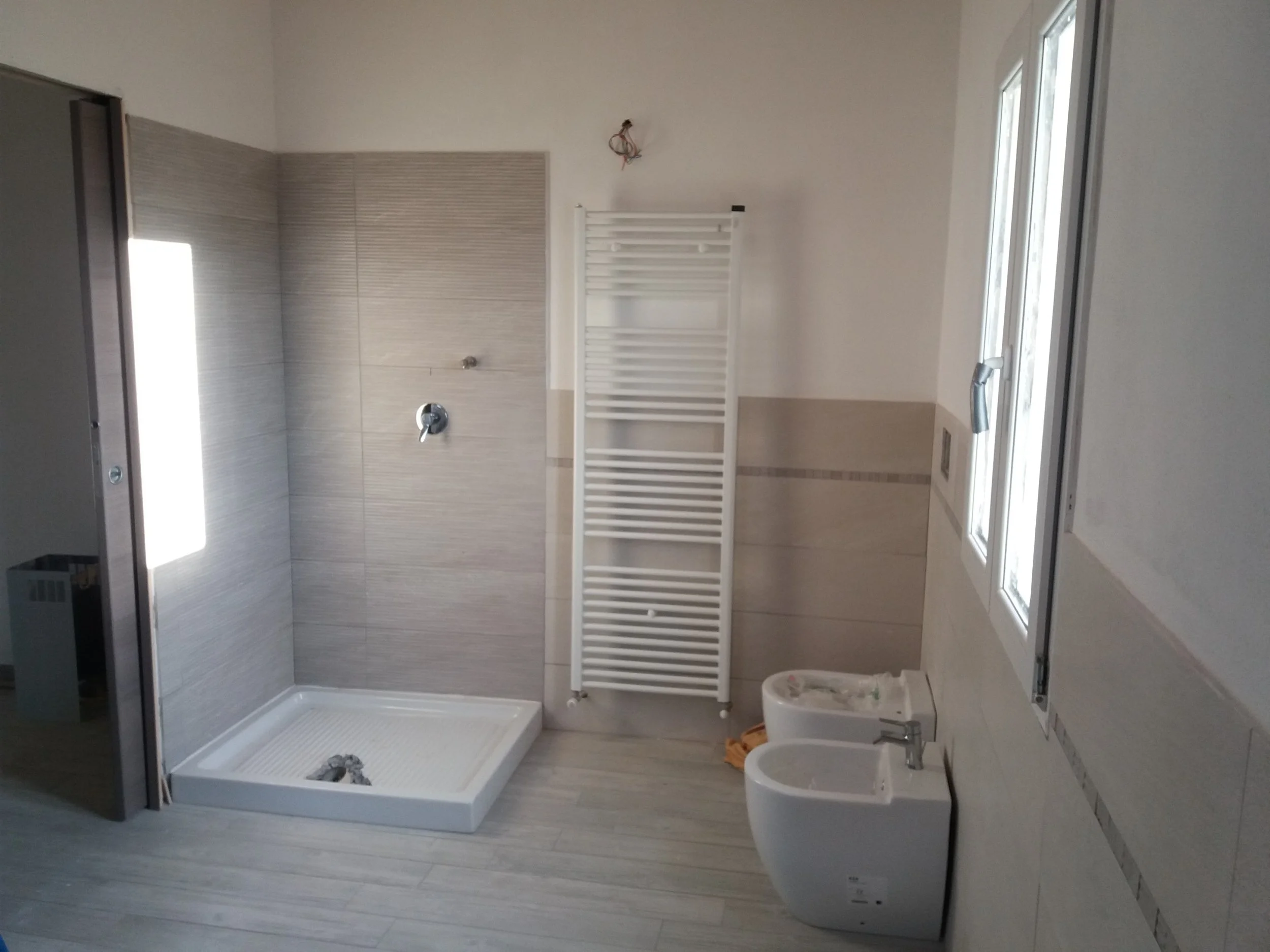 Bathroom under renovation with a shower, a white radiator, a bidet, and a window.