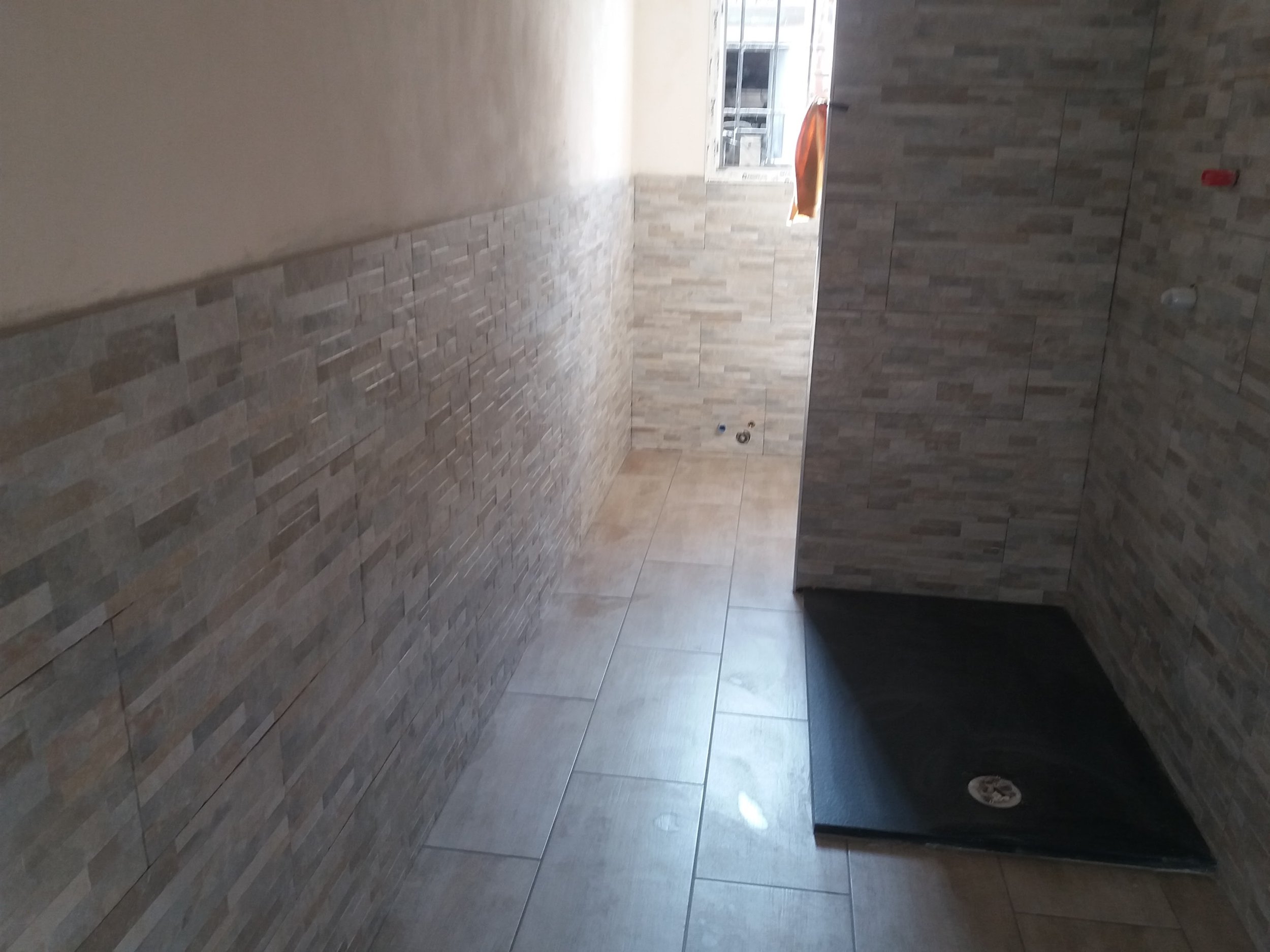 An unfinished interior space with tiled walls and floor, with some pipes and fixtures visible, possibly a bathroom or kitchen under construction.