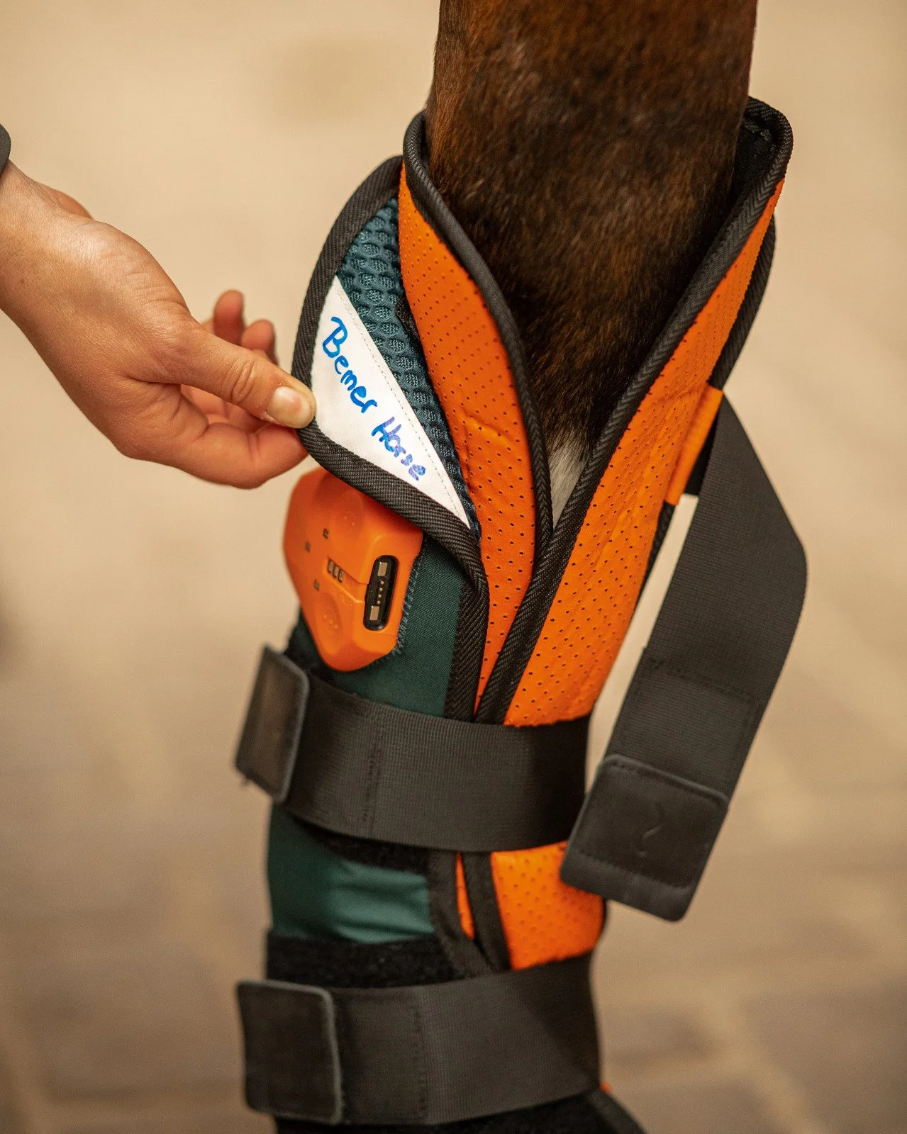 Person trägt eine orange Sicherheitsweste mit Gehörschutz. Eine Hand legt eine kleine weiße Flagge mit blauer Unterschrift auf die Weste. Die Unterschrift lautet 'Bemer Heli'.