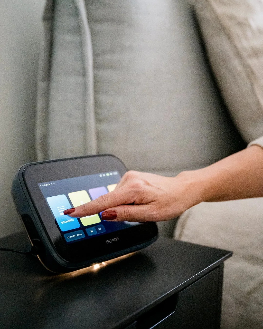 Nahaufnahme einer Hand mit roten Nägeln, die einen Touchscreen-Controller berührt, der auf einem schwarzen Tisch steht.