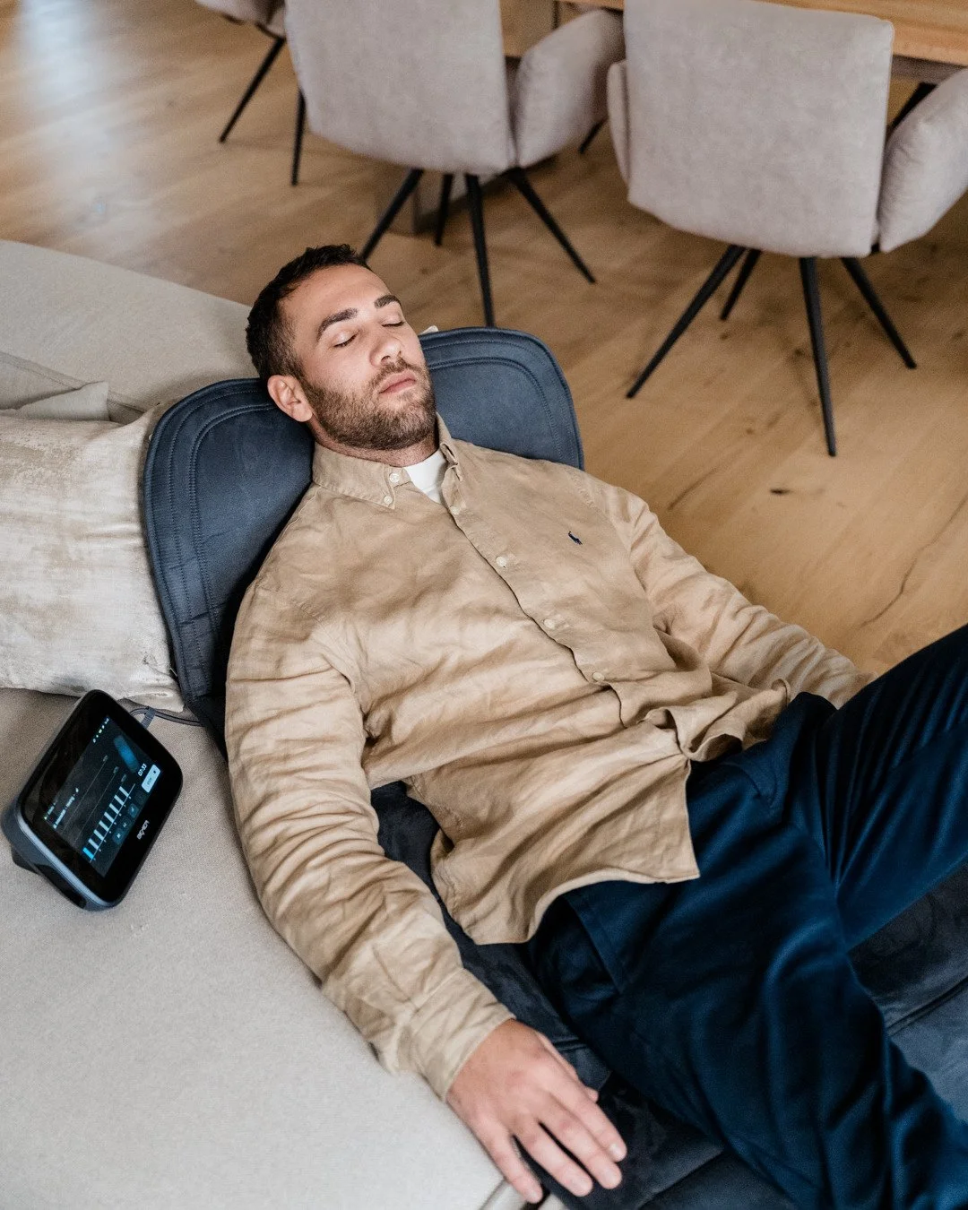 Ein Mann liegt entspannt auf einer Couch und schläft, neben ihm ein medizinisches Gerät, vermutlich ein Überwachungsmonitor.
