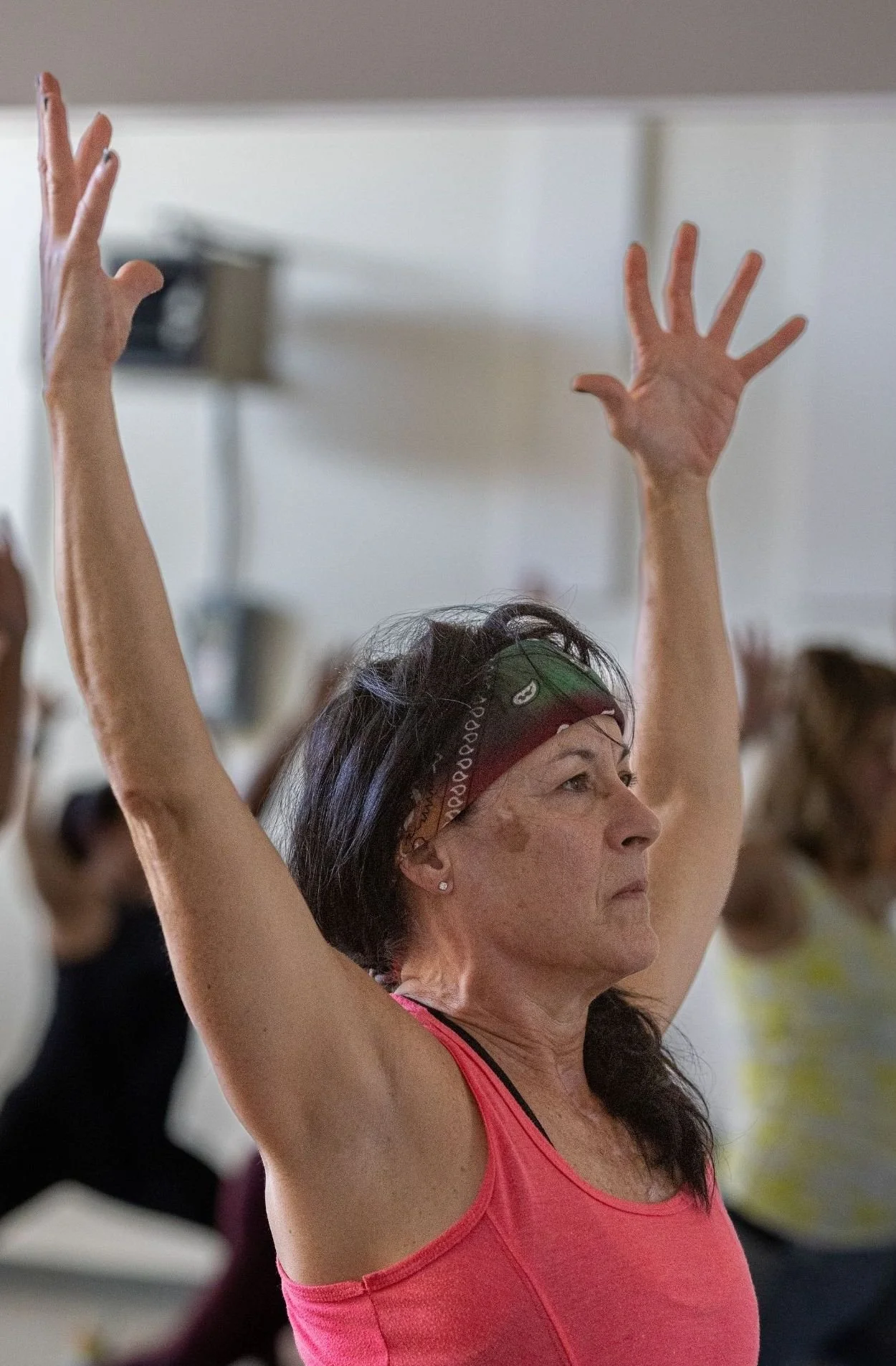 A woman in a pink athletic top raising her arms during a fitness class or exercise session.