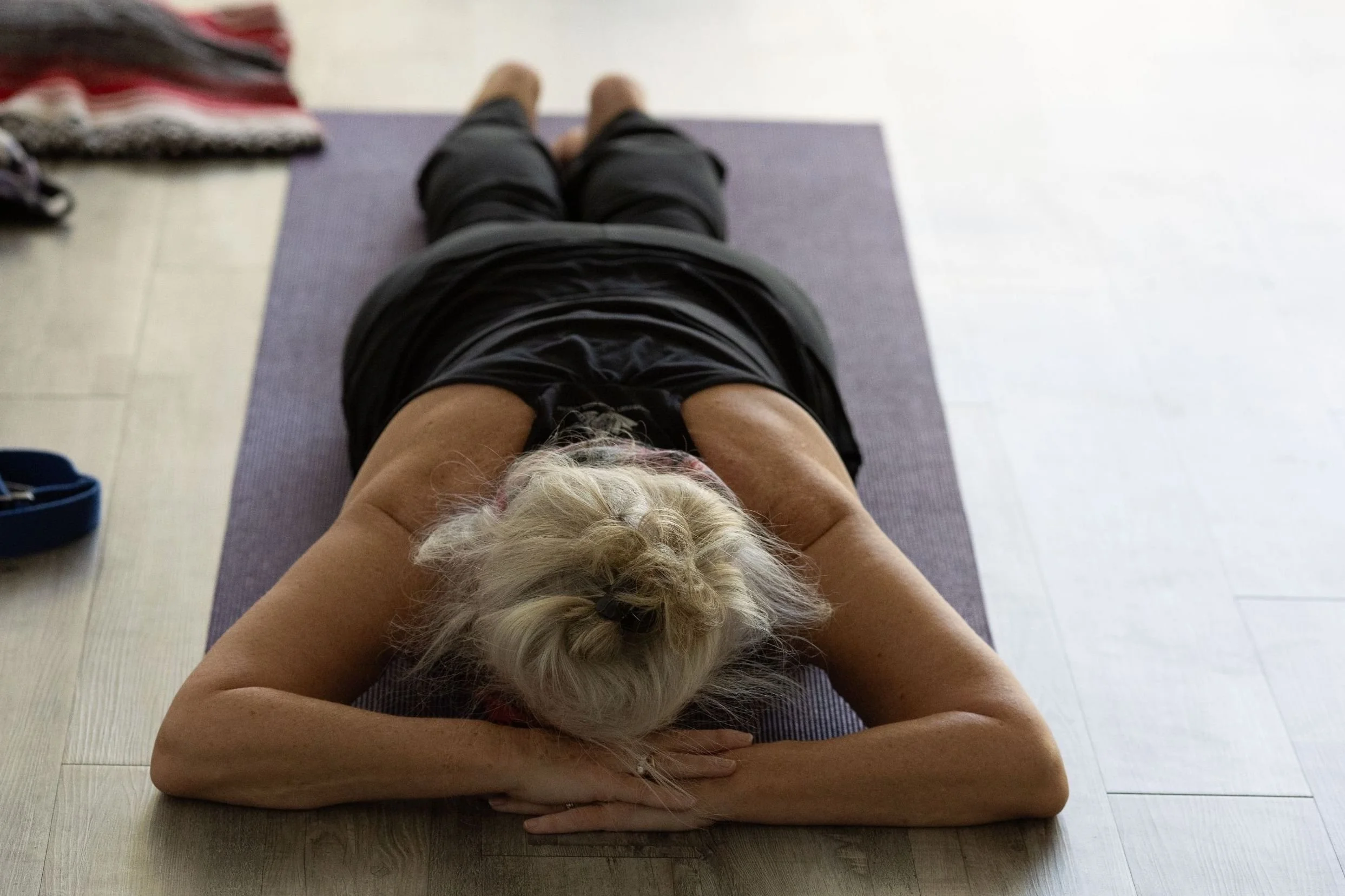 Person lying on a yoga mat doing a stretch or yoga pose, with a small dog lying on their chest.