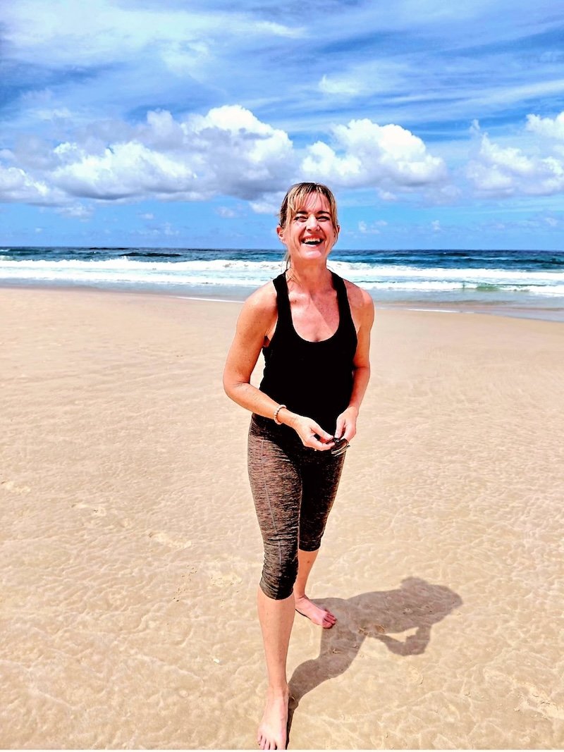 Woman laughing on a sandy beach representing the energy and confidence that comes from personalised metabolic weight loss