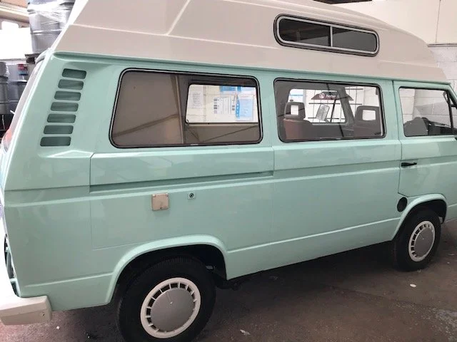 A mint green vintage camper van with a white high roof, parked indoors.