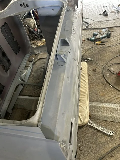 Close-up of an empty metal appliance, likely a washing machine or dryer, on a workshop floor with tools and wires scattered around.