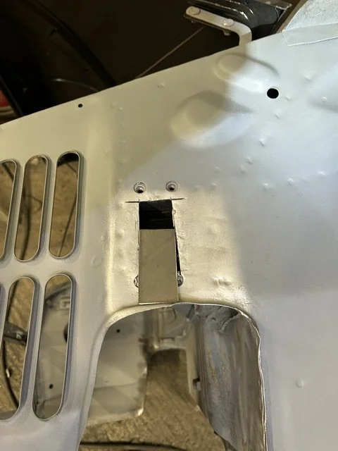 Close-up of a metallic aircraft or drone with several drilled holes and a rectangular opening, showing part of its structural frame.