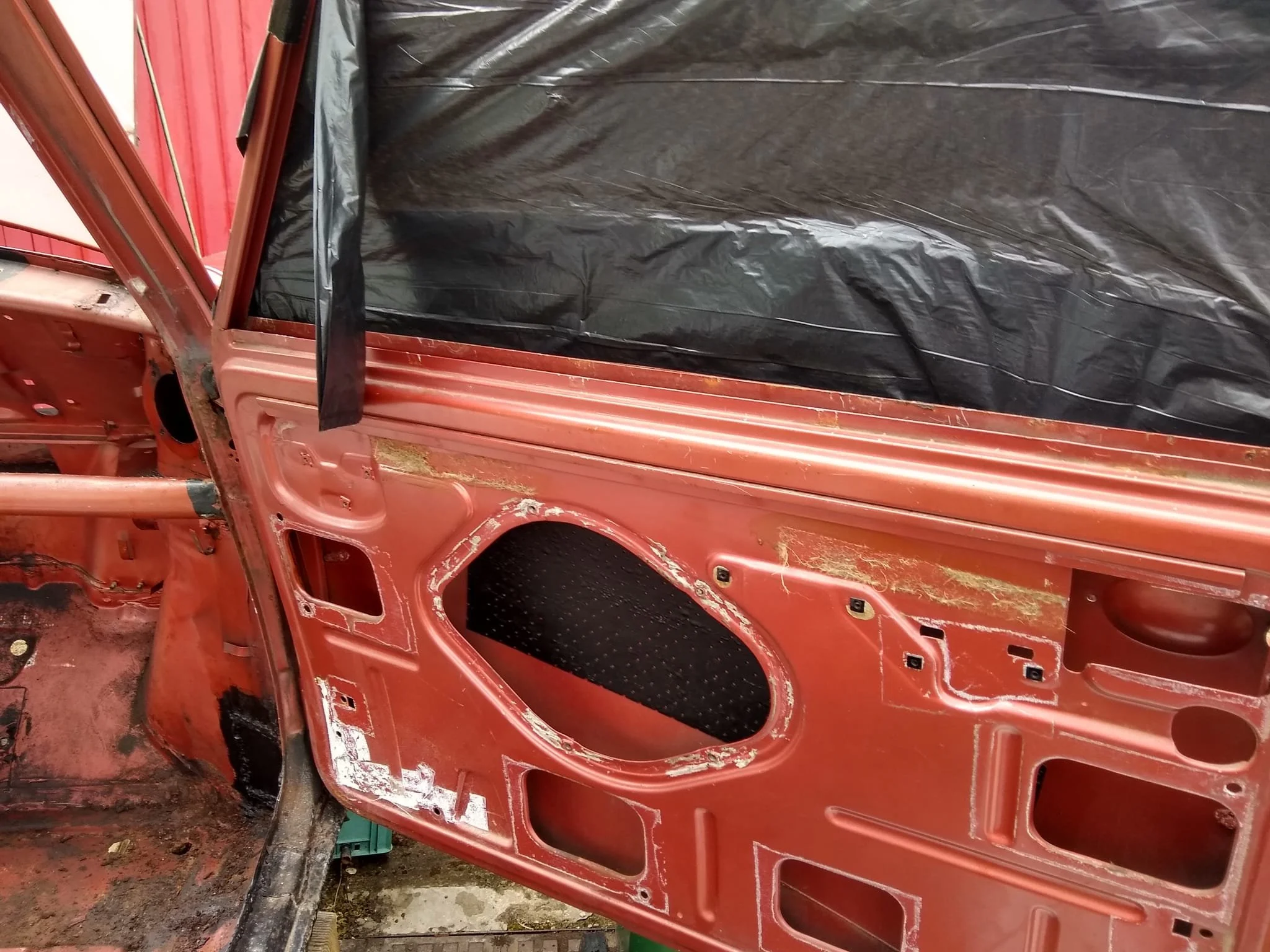 A partially disassembled red car with internal panels missing, exposing the inner structure and wiring, with a black plastic sheet covering some parts.