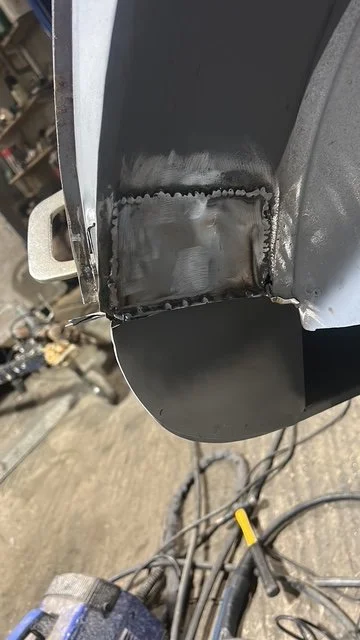 Close-up of a metal welding repair on a curved metal surface, showing a welded seam with some finishing work.