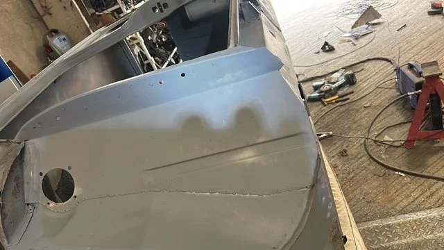 Partially assembled metal vehicle body on a workbench with tools and equipment in the background.