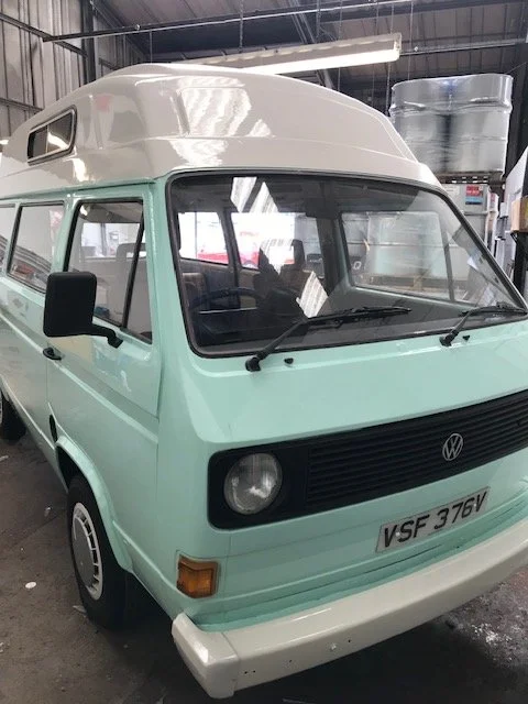 Mint green Volkswagen camper van with a white roof parked inside a warehouse.