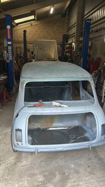 Empty vintage car body inside a garage with car lift in the background.