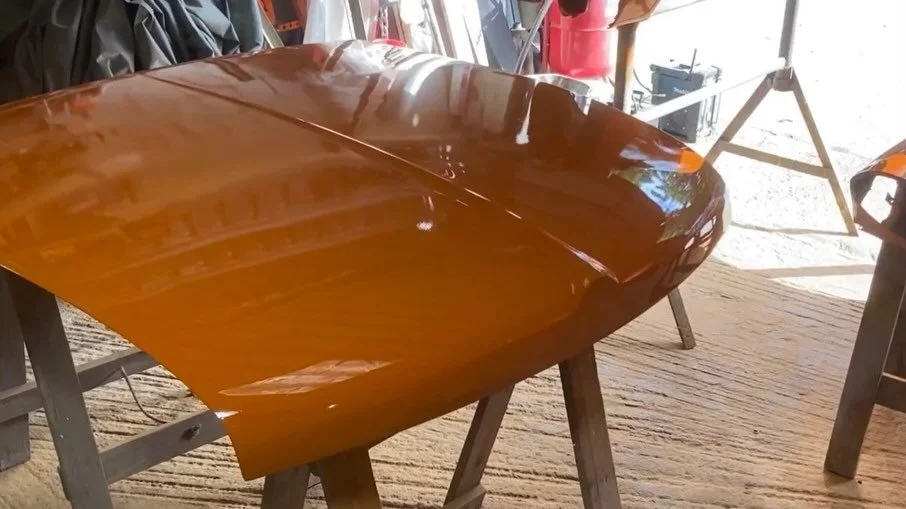 A car hood painted in a glossy metallic copper color, mounted on a wooden stand inside a workshop.