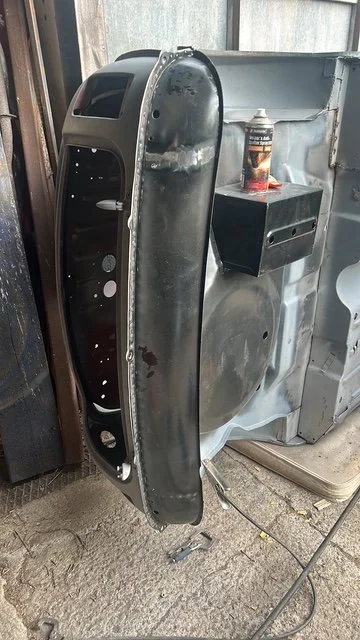 An old, partially disassembled car dashboard placed upright against a washing machine in a garage. The dashboard appears worn and is missing some components.